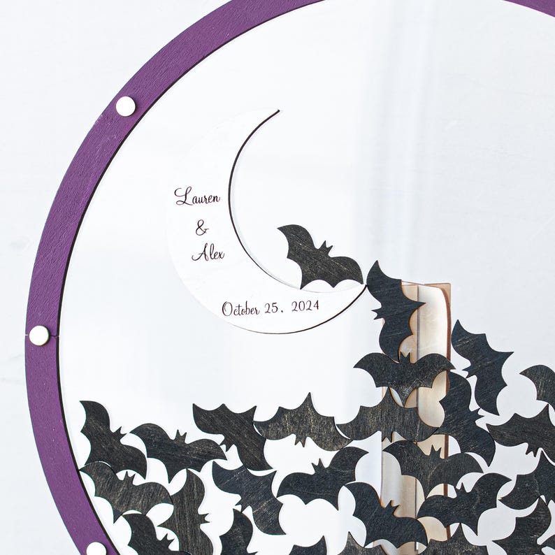 Close-up of personalized Gothic wedding guest book with engraved names and bat tokens. Elegant acrylic and plywood frame for a halloween-themed wedding.