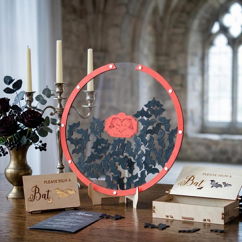 May include: A circular clear acrylic guest book frame with a red border, filled with small black wooden bat cutouts. A central red plaque features engraved text. Includes a wooden sign reading "PLEASE SIGN A Bat" and a matching wooden box.