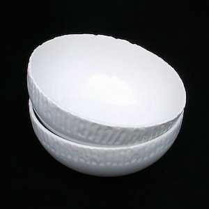 May include: Two white ceramic bowls stacked on top of each other. The bowls have a textured, ribbed design around the rim.