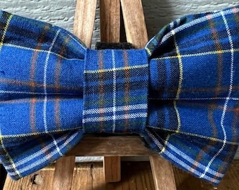 May include: A blue plaid bow tie with yellow, white, and orange stripes. The bow tie is displayed on a wooden easel.