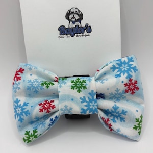 May include: A light blue and white bow tie with a snowflake pattern in red, green, and blue. The bow tie is from Baylor's Bow Tie Boutique.