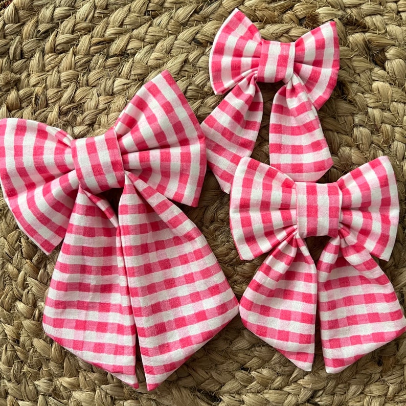 May include: Three pink and white gingham bows of varying sizes. The bows are tied with a loop and are perfect for adding a touch of whimsy to any project.
