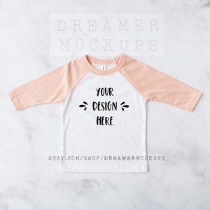 May include: A white long-sleeve baseball tee with peach colored sleeves. The shirt has a blank area on the front that says "Your Design Here".