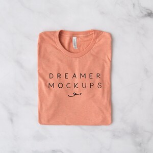 May include: A folded coral coloured t-shirt with the text "DREAMER MOCKUPS" printed on the front.