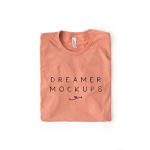 May include: A folded coral coloured t-shirt with the text "DREAMER MOCKUPS" printed on the front.