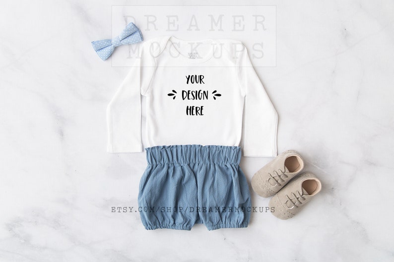 May include: White long-sleeved baby bodysuit with the text 'YOUR DESIGN HERE' on the front. The bodysuit is paired with blue denim shorts and beige baby shoes.