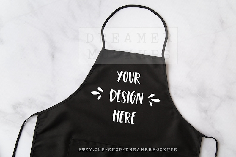 Może przedstawiać: Czarny fartuch z białym tekstem, kt&oacute;ry m&oacute;wi "Your Design Here" na białym marmurowym tle.