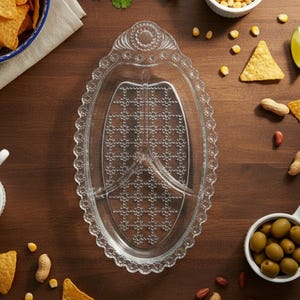 May include: Clear, oval-shaped serving platter with three compartments and a decorative scalloped edge. The platter is surrounded by snacks like tortilla chips, peanuts, olives, and corn kernels, suggesting a party or gathering.