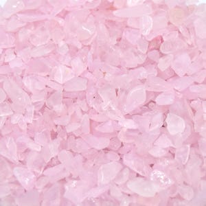 Op de afbeelding: Een close-up van een grote hoeveelheid kleine, roze rozenkwarts chips. De chips zijn onregelmatig gevormd en hebben een doorschijnende uitstraling.