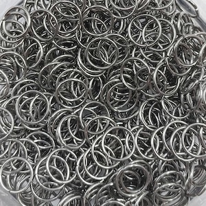 Peut inclure: Gros plan sur un tas de anneaux de saut métalliques argentés et brillants. Les anneaux sont circulaires, avec une fente dans chaque anneau, et sont densément emballés. Ces anneaux sont probablement utilisés pour la fabrication de bijoux ou de cotte de mailles.