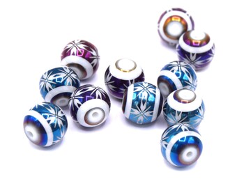 May include: A collection of round, iridescent blue and purple beads with white snowflake designs. The beads are scattered on a white surface.