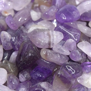 Può includere: Primo piano di una ciotola piena di pietre di ametista levigate. Le pietre sono di varie tonalità di viola e hanno una finitura liscia e lucida.