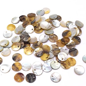 Könnte beinhalten: Eine Sammlung runder, irisierender Muschelkugeln mit einem Loch in der Mitte. Die Kugeln sind in Weiß-, Braun- und Goldtönen gehalten.