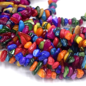 Könnte beinhalten: Eine Strähne aus bunten, unregelmäßig geformten Muschelperlen. Die Perlen sind in Rot-, Orange-, Gelb-, Grün-, Blau- und Violetttönen gehalten.