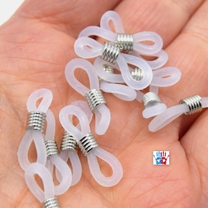 May include: A close-up of a pile of white plastic eyeglass end tips with silver metal rings. The end tips are designed to attach to the ends of eyeglass chains or cords.
