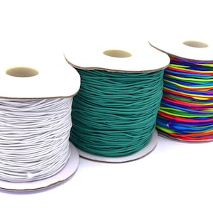 Pode incluir: Três rolos de cordão elástico, um branco, um verde-azulado e um com um arco-íris de cores.