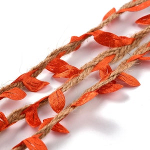 Op de afbeelding: Close-up van drie strengen decoratief touw met oranje stoffen bladeren. Het touw heeft een natuurlijke bruine kleur en de bladeren zijn fel oranje. De bladeren zijn gelijkmatig verdeeld over het touw.