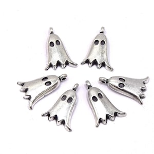 Op de afbeelding: Zeven zilveren spookbedels, elk met twee zwarte ogen. De bedels zijn in de vorm van een spook met een afgeronde bovenkant en een puntige onderkant. De bedels zijn in een cirkel op een witte achtergrond gerangschikt.