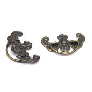 May include: Two ornate bronze drawer pulls with a decorative design. The pulls have a ring shape for easy gripping.