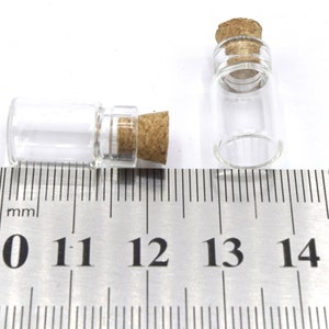 May include: Two small clear glass bottles with cork stoppers, measured against a ruler in millimeters. The bottles are approximately 11 millimeters in diameter and 25 millimeters in height.