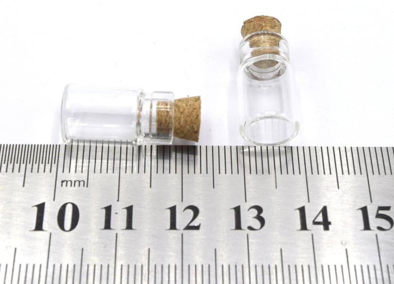 May include: Two small clear glass bottles with cork stoppers, measured against a ruler in millimeters. The bottles are approximately 11 millimeters in diameter and 25 millimeters in height.