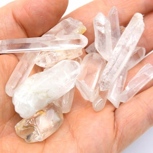 Peut inclure: Une collection de pointes de cristal de quartz clair, également connues sous le nom de cristaux de roche, de différentes tailles et formes. Les cristaux sont disposés en pile sur la main d'une personne.