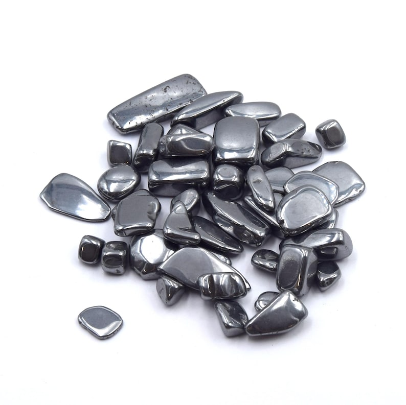 Peut inclure: Un tas de pierres d'h&eacute;matite polies, de couleur gris fonc&eacute;. Les pierres ont des formes vari&eacute;es, de rondes &agrave; rectangulaires, et une surface lisse et r&eacute;fl&eacute;chissante. Les pierres sont dispers&eacute;es sur un fond blanc.