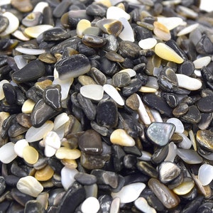 May include: A close-up of a pile of black, white, and brown stones. The stones are small and smooth, and they appear to be made of natural materials.