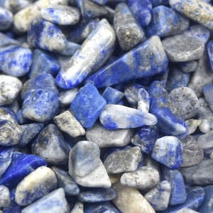 Może przedstawiać: Zbliżenie na stos małych, niebieskich i białych, polerowanych kamieni lapis lazuli. Kamienie mają nieregularny kształt i r&oacute;żne rozmiary.