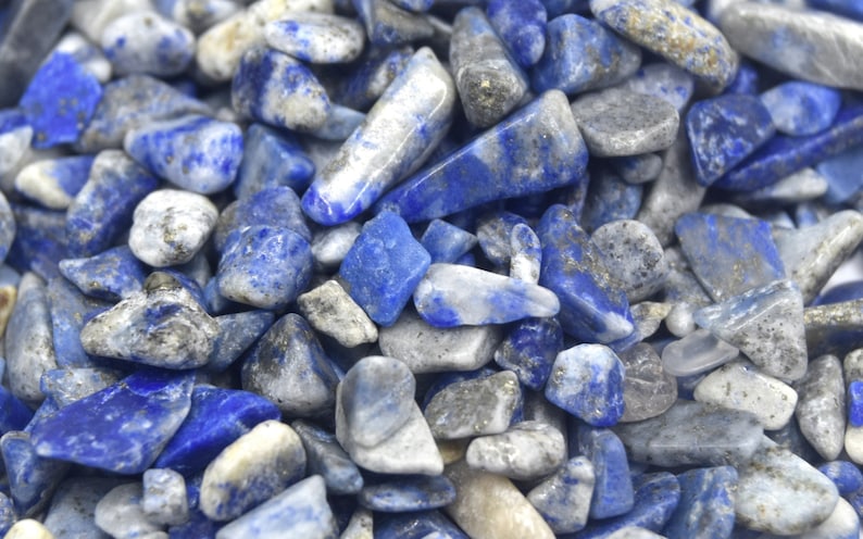 Może przedstawiać: Zbliżenie na stos małych, niebieskich i białych, polerowanych kamieni lapis lazuli. Kamienie mają nieregularny kształt i r&oacute;żne rozmiary.