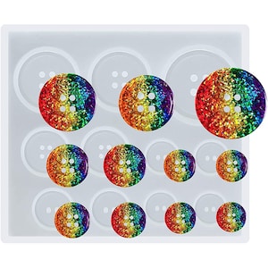 Könnte beinhalten: Eine Silikonform zum Herstellen von Regenbogen-Glitzerknöpfen. Die Form hat 10 Vertiefungen in verschiedenen Größen. Die Form ist weiß und die Knöpfe sind regenbogenfarben mit Glitzer.