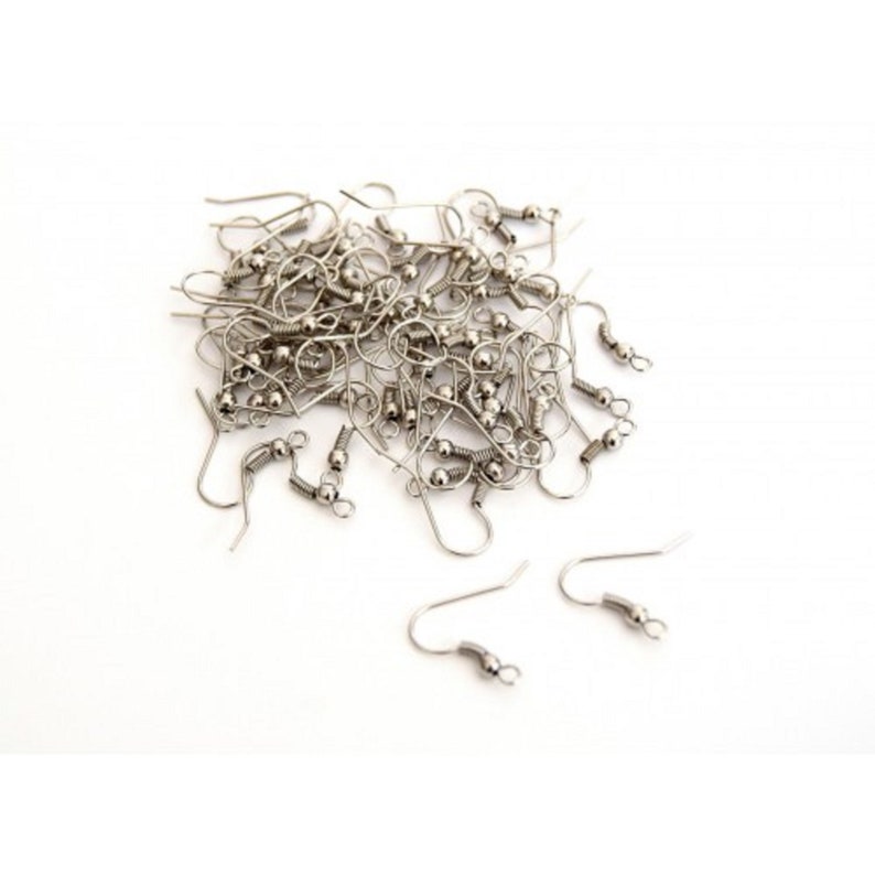 May include: A pile of silver earring hooks with a ball at the top. The hooks are scattered on a white surface.