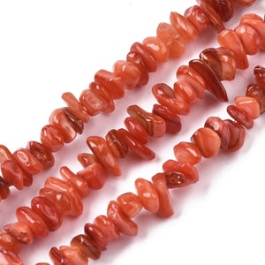 Può includere: Una collana di perline di pietra preziosa di forma irregolare di colore arancione e rosso. Le perline sono piatte e hanno una finitura lucida.
