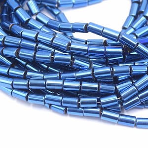 Peut inclure: Un brin de perles métalliques bleues, chaque perle est un cylindre avec un bord légèrement arrondi. Les perles sont disposées en un tas lâche, montrant l'éclat métallique des perles.