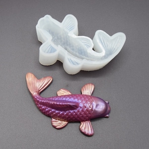 K&ouml;nnte beinhalten: Eine Silikonform zum Herstellen eines violetten Koi-Fischs. Die Form ist ge&ouml;ffnet und ein fertiger Koi-Fisch aus Harz ist daneben abgebildet.