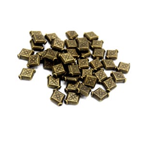 May include: A pile of antique gold square beads with a floral design. The beads are about 1 cm in size.