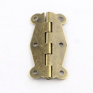 Könnte beinhalten: Antike Messing Scharnier mit dekorativem Design. Das Scharnier hat eine patinierte Oberfläche und ist geeignet für den Einsatz an Möbeln, Schränken oder anderen Projekten.