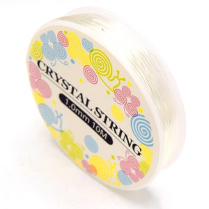 Può includere: Un rotolo di filo elastico trasparente per la creazione di gioielli. L'etichetta recita "Crystal String 1.0mm 10M".