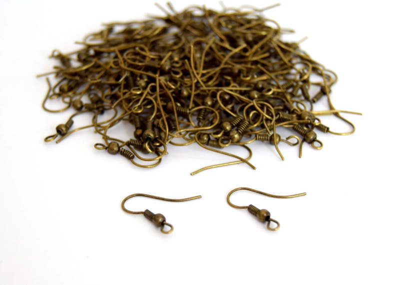 May include: A large pile of gold-toned earring hooks. The hooks are made of metal and have a small loop at the top. There are two individual hooks in the foreground.