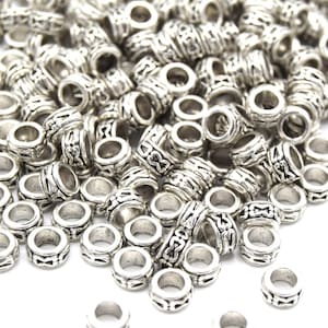 Könnte beinhalten: Ein großer Haufen silberner Metallperlen mit einem komplizierten Design. Die Perlen sind rund und haben ein Loch in der Mitte.
