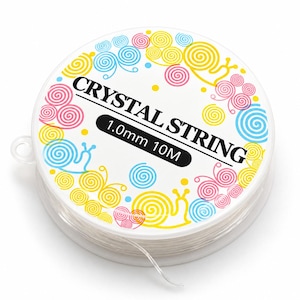 Pode incluir: Uma bobina redonda de cordão elástico transparente com o rótulo CRYSTAL STRING 1.0mm 10M. O rótulo branco apresenta um padrão colorido de caracóis amarelos, rosas e azuis com conchas em espiral em torno do texto preto.