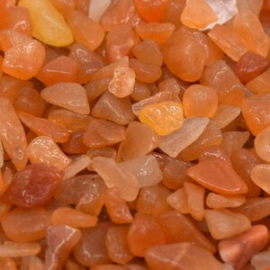 Peut inclure: Gros plan sur un tas de petites pierres de cornaline orange. Les pierres sont lisses et polies, et elles ont une qualité translucide.