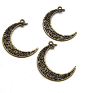 Peut inclure: Trois breloques en métal doré antique en forme de croissant de lune avec des motifs filigranés complexes.