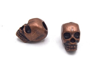 May include: Two copper skull beads with detailed features. The beads are approximately 1 inch in diameter.