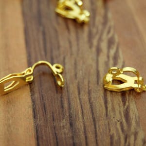 Peut inclure: Trois fermoirs d'oreille dorés sur une surface en bois. Les fermoirs sont conçus pour maintenir les boucles d'oreilles en place.