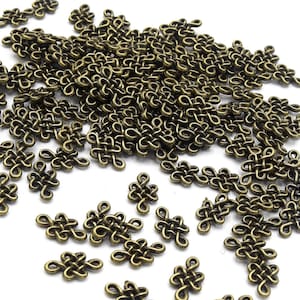 May include: A large quantity of small, antique gold-colored metal charms in the shape of a knot. The charms are scattered on a white surface.