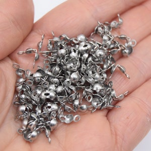 May include: A pile of silver metal bead caps with a loop on one end and a small ball on the other end.