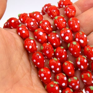 Può includere: Un filo di perline di vetro rosso con pois bianchi e accenti verdi. Le perline hanno la forma di fragole.