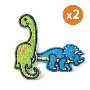 May include: Two dinosaur patches. One is a green Brontosaurus with orange spots and the other is a blue Triceratops. Both have black and yellow accents. A circular orange sticker with the text "x2" is in the upper right corner.