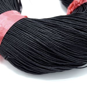 May include: A close-up of a spool of black waxed cotton cord. The cord is tightly wound and has a smooth, polished finish.
